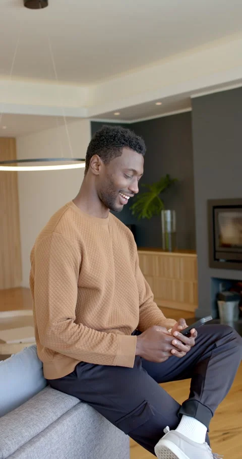 Vertical video: Man tapping smartphone on sofa, reading funny content and Stock Footage 345395692
