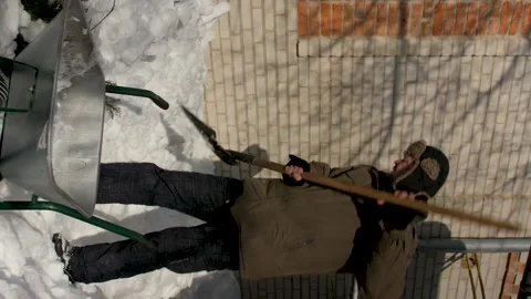 Vertical video. A man throws a snow shovel into a metal wheelbarrow under house. Video stock 220132311