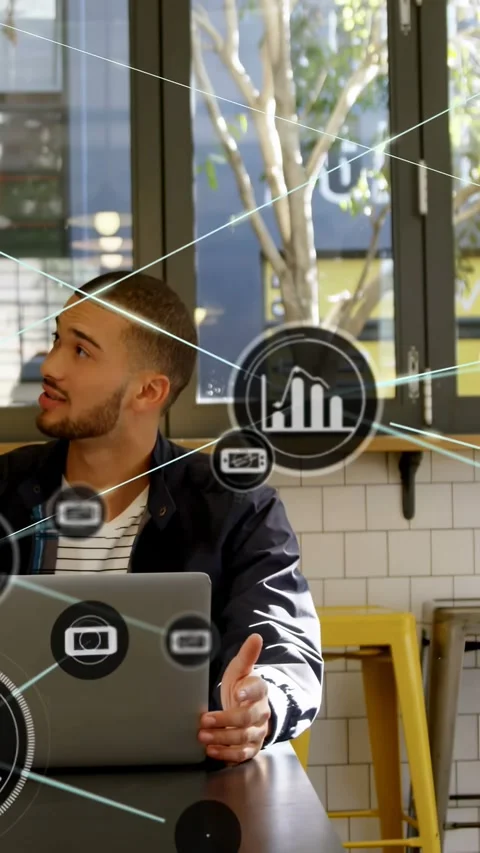 Vertical video: Man typing and gesturing on laptop in cafe, HUD icons forming to Stock Footage 334540805