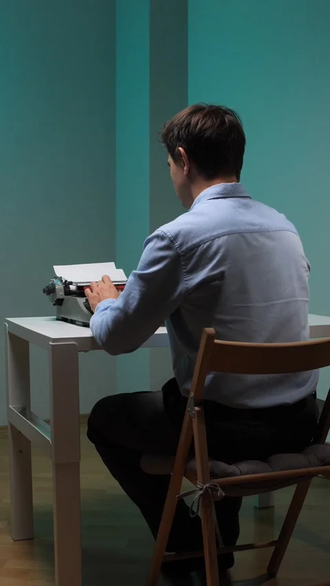 Vertical video man typing on a classic manual typewriter at a simple white Stock Footage 345532162