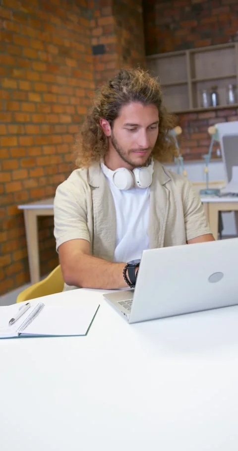 Vertical video: Man typing on laptop at co-working desk, pausing and responding Stock Footage 342035836