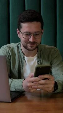 Vertical video. Man using smartphone and laptop in coffee shop. Foto stock
