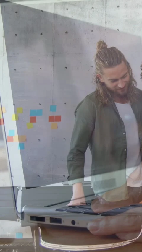 Vertical video: Man working on laptop coworker entering both reviewing office Stock Footage 333541845
