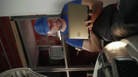 Vertical video: A mechanic wearing a blue cap uses a laptop to diagnose an issue Stockbeeldmateriaal 280378043