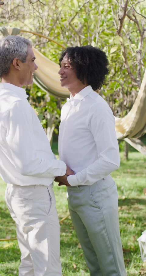 Vertical video: Men in white shirts holding hands meeting gaze smiling at Stock Footage 345397195
