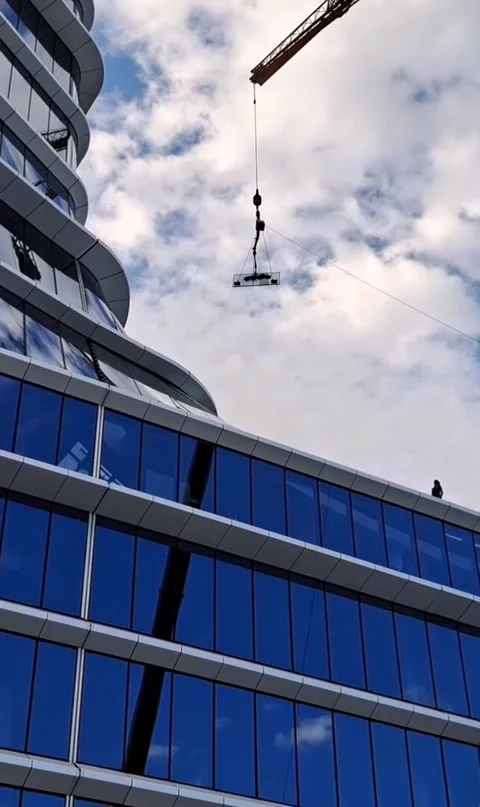Vertical video of mobile crane hoisting glass panel into high-rise Stock Footage 337359378