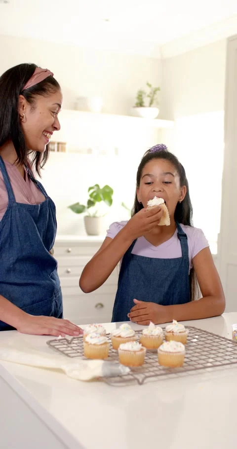 Vertical video: Mom in apron handing cupcake guiding girl tasting treat at 動画素材 346724159