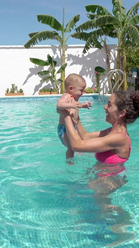 Vertical video of a mom playing with her baby in the pool for the first time, Stockbeeldmateriaal 220351688