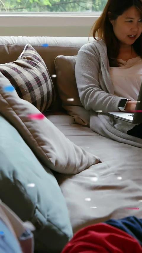 Vertical video: Mom on sofa working on laptop while child climbing and needing Stock Footage 333913114