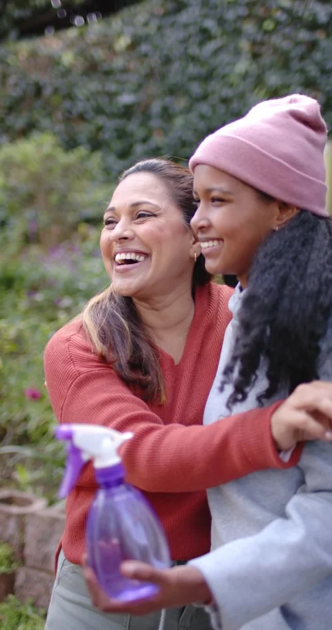 Vertical video: Mother pulling daughter close, posing while holding spray bottle Stock Footage 337734485