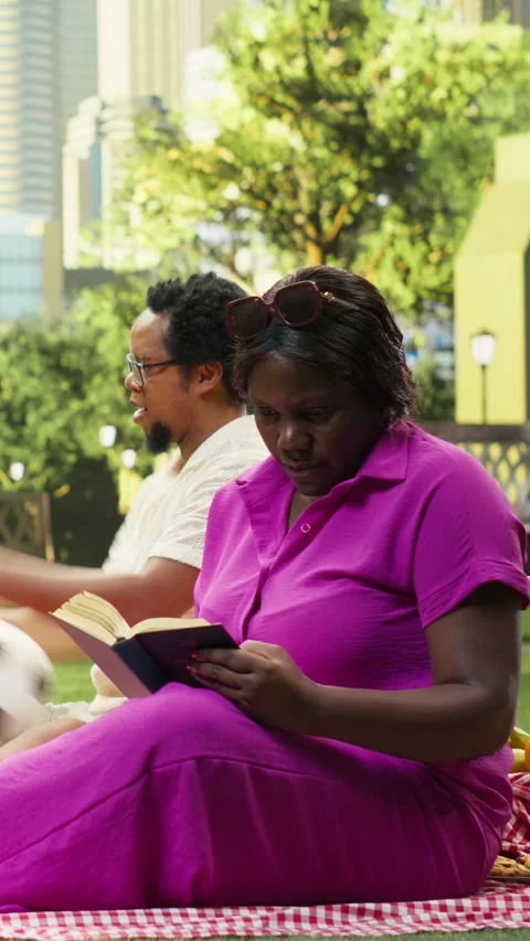 Vertical Video Mother reading book on checkered picnic blanket while boy and dad Stock Footage 341471112