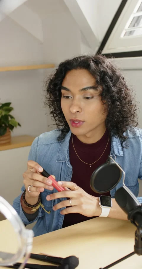 Vertical video: Non-binary creator lifting red gloss tube at loft desk, twisting Stock Footage 345395281
