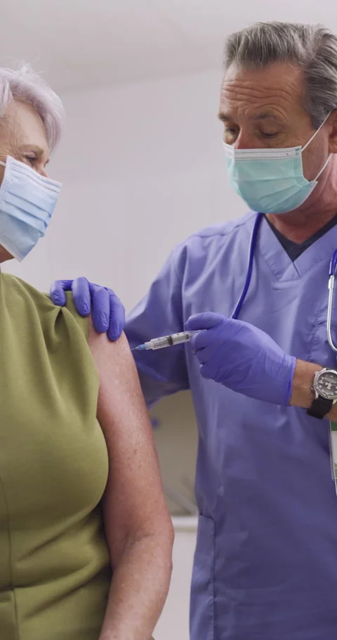 Vertical Video. A Nurse Administers A Covid-19 Vaccine To An Elderly Patient Stock Footage 154904137