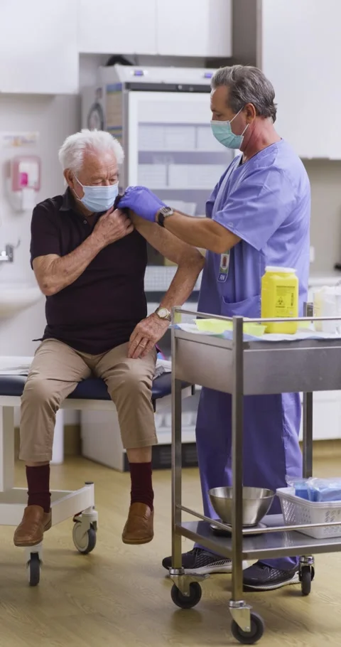 Vertical Video. A Nurse Administers A Covid-19 Vaccine To An Elderly Patient Stock Footage 155553760