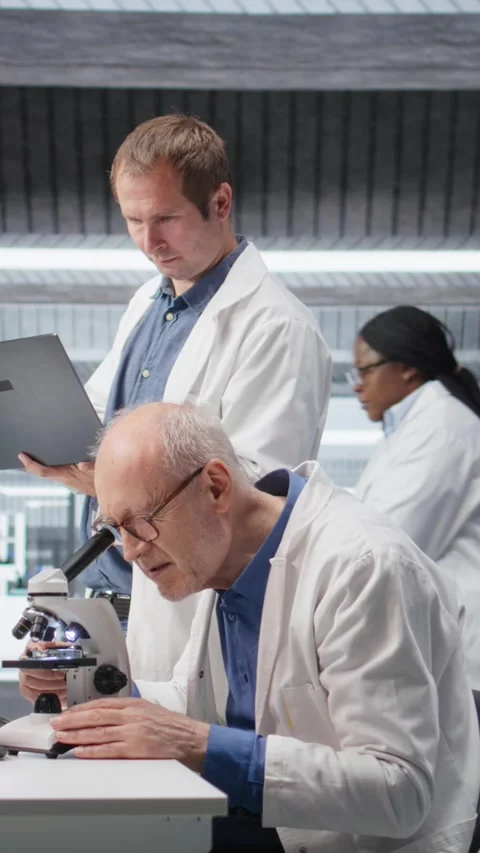 Vertical Video Old man scientist using microscope with a colleague for clinical Stock Footage 317733005