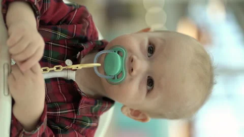 Vertical video. one-year-old boy in a red shirt and a pacifier in his mouth sits 動画素材 219744869