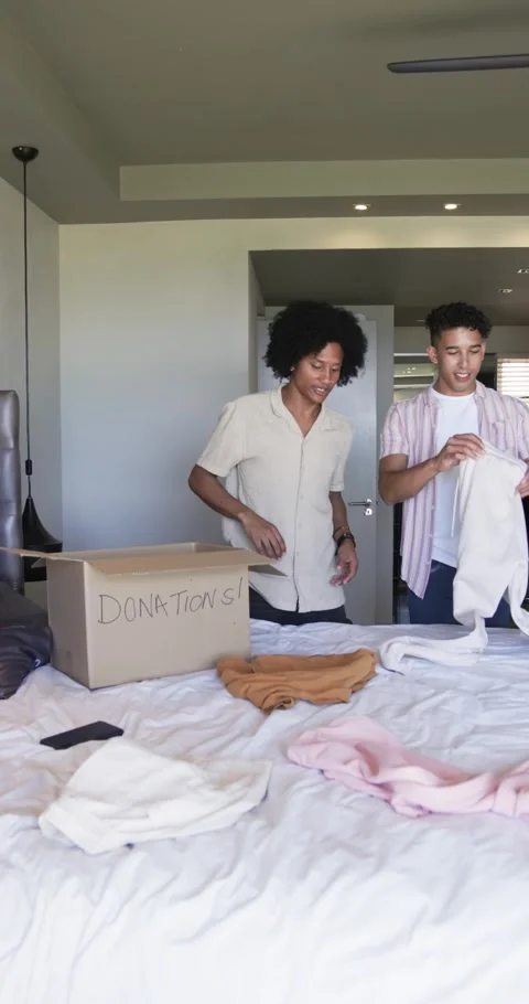 Vertical video: Opening donations box, two friends sorting clothes on bed, Stock Footage 345492846