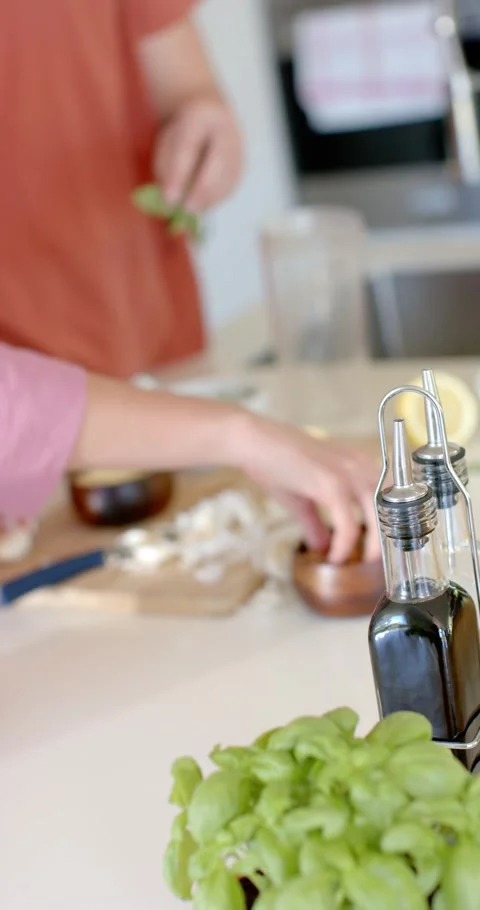 Vertical video: Orange shirt is reaching, hands are tearing basil, adding nuts Stock Footage 345040632