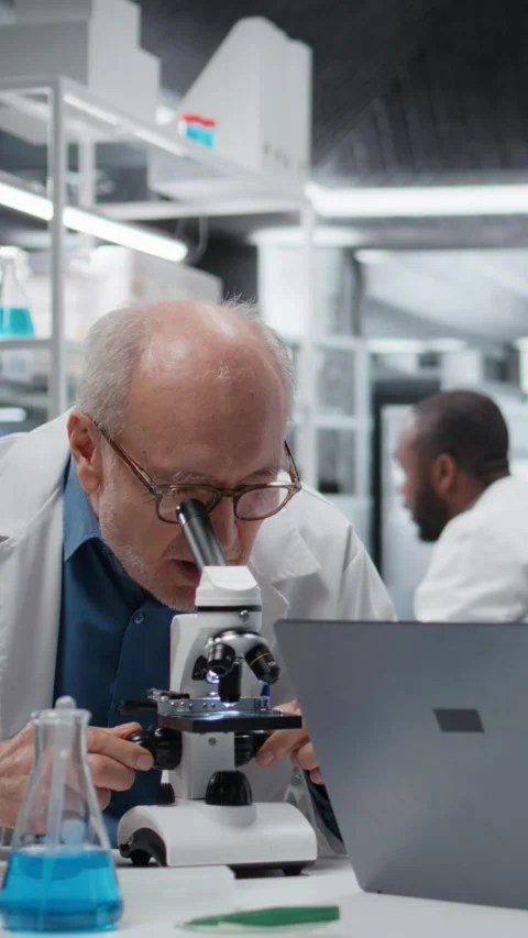 Vertical video Pathologist examining biopsy slide while coworker documents Stock Footage 325681106