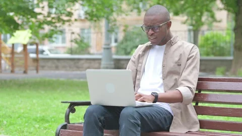 Vertical Video, Perplexed Young African Man Using Laptop on Park Bench Stock Footage 310832535