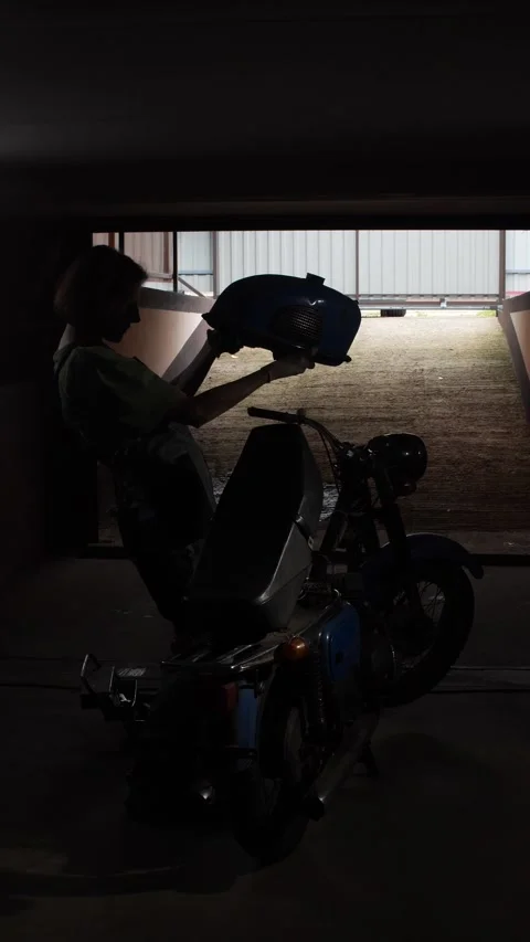Vertical video person is sitting on a moped in a dark parking garage, putting Stock Footage 340429445