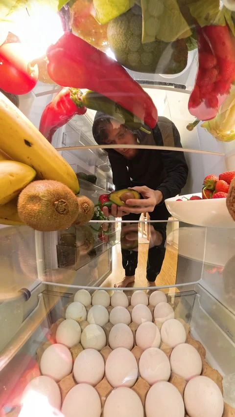 Vertical video. A perspective from inside a refrigerator shows a man looking Stock Footage 293297251