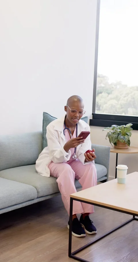 Vertical video: Phone pinging African woman in scrubs grabbing apple checking Stock Footage 346723987