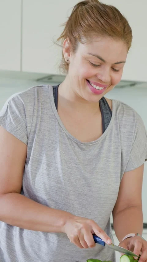 Vertical video: Picking up blue knife, woman preparing and tasting cucumber in Stock Footage 348369968