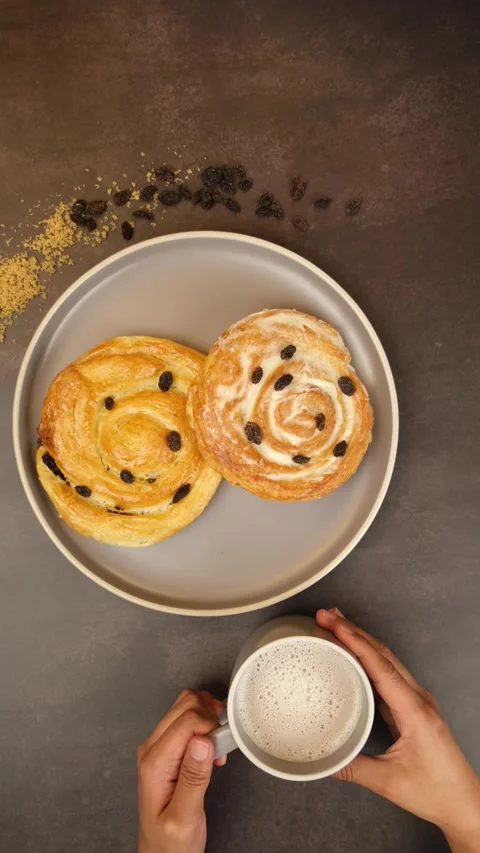 Vertical video Placing a cup of creamy latte next to a plate of sweet bread Stock Footage 279355094