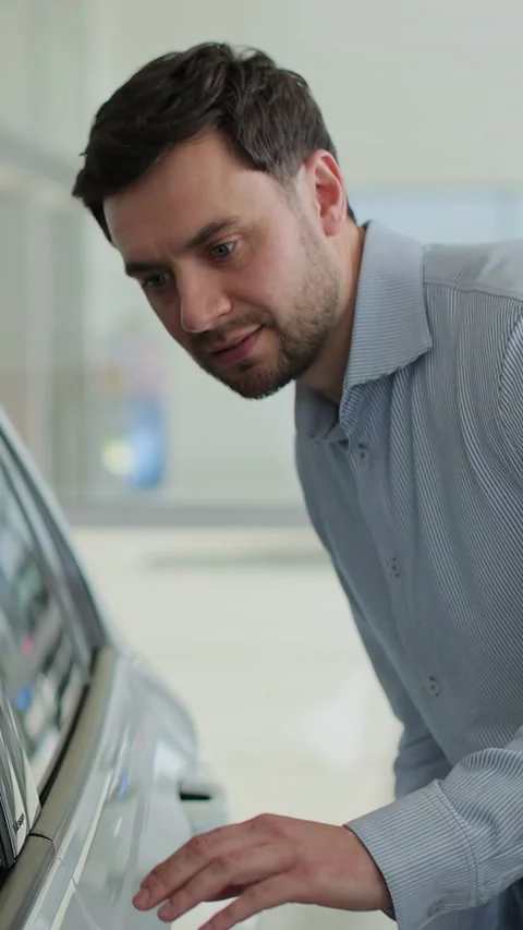 Vertical video Portrait of handsome man touching new car in showroom. Stock Footage 337239561