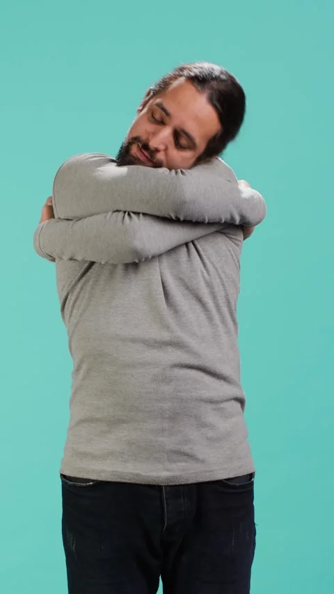 Vertical video Portrait of man standing in studio, hugging himself, doing self Stock Footage 314514989