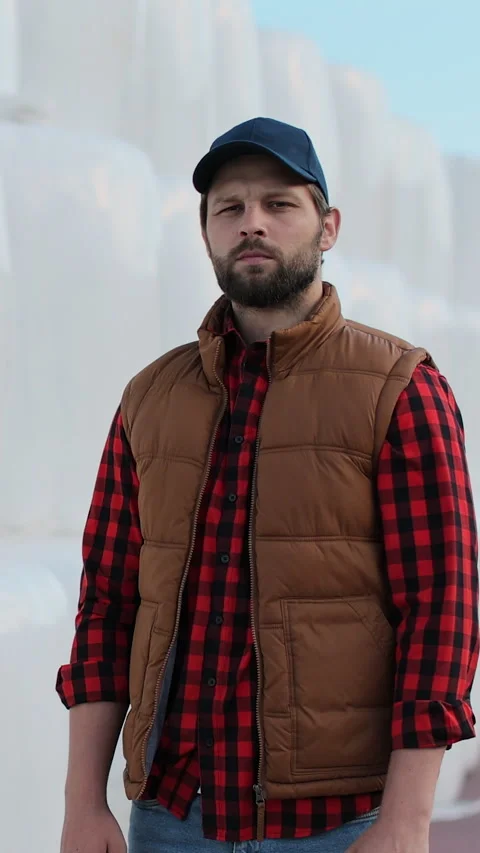 Vertical video. Portrait of a young farmer in work attire posing by hay stack. Stock Footage 344630516