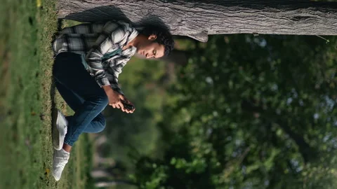 VERTICAL VIDEO POV relaxed Hispanic guy use smartphone sitting at summer sunny Vídeo Stock 219960932