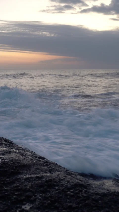 Vertical video of Powerful ocean waves crashing on rocky coastline at sunset Stock Footage 332228074