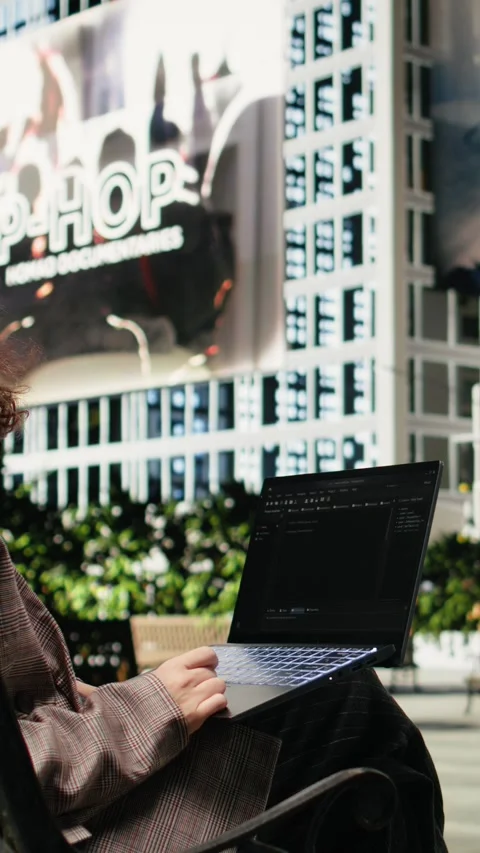 Vertical video Programmer writing code on laptop while sitting on park bench Video stock 343559306