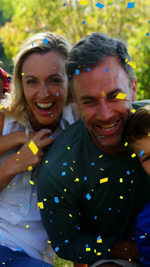 Vertical video: Pullback showing family on lawn, piggyback child, confetti, Stock Footage 332547108
