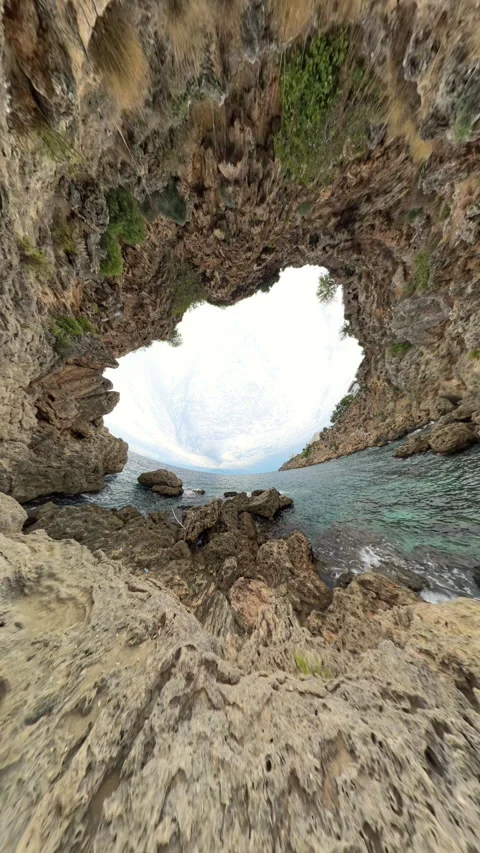 Vertical video. Rabbit Hole Planet. A rocky coastal cave frames a view of the Stock Footage 287901175