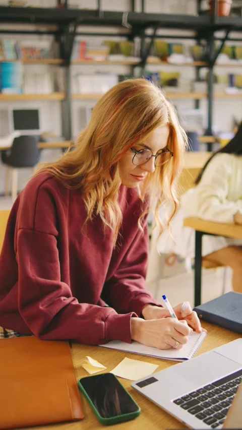 Vertical video of red-haired female student in glasses sits in the foreground Stock Footage 294714191