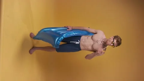 Vertical video of Red-haired man in beach shorts with an inflatable mattress and Stock Footage 200834500