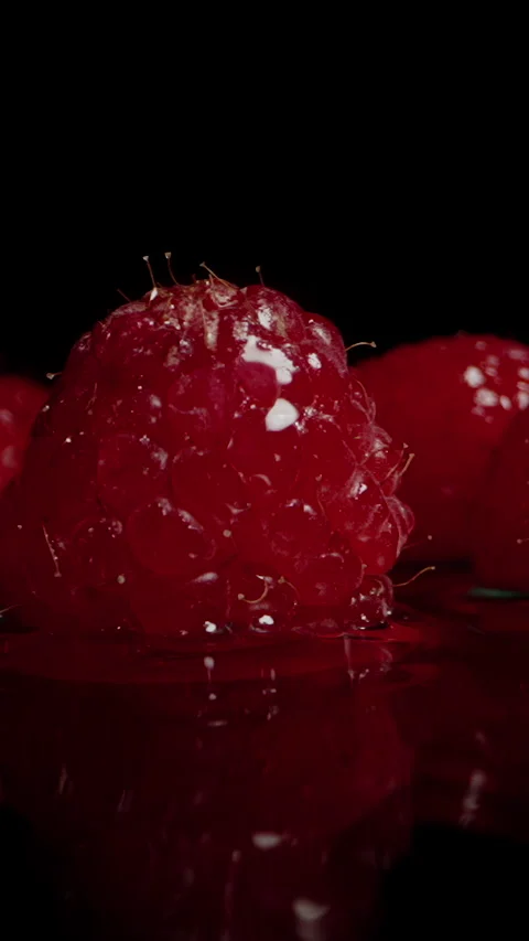 Vertical video. Red raspberry berries falling onto a wet black surface, splashin Stock Footage 270425639