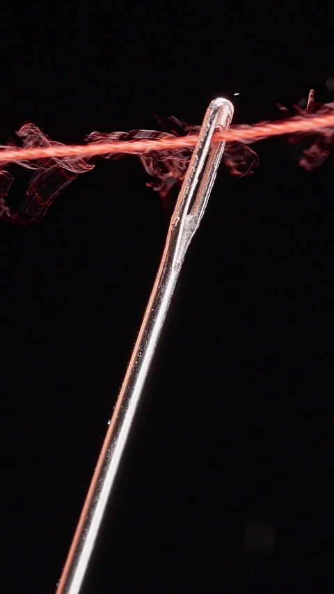 Vertical video. Red Thread Passes Through a Metal Needle Eye Against a Black Bac Stockbeeldmateriaal 341416240