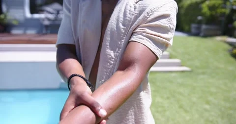 Vertical video: Rubbing man smoothing right forearm at backyard pool, wearing Stock Footage 343838832