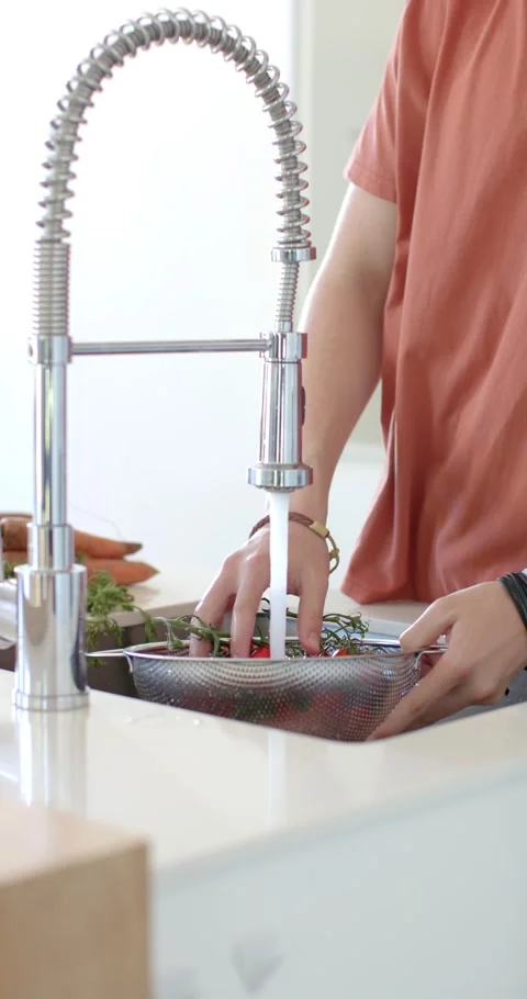 Vertical video: Running faucet is starting cook rinsing tomatoes in strainer at Stock Footage 345396403