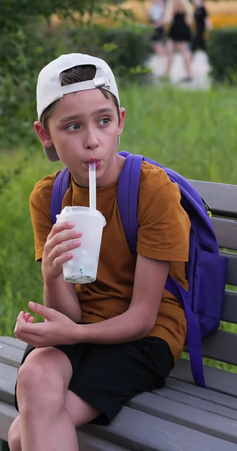 Vertical video of school boy drinking milkshake on bench. Student boy with Stock Footage 328706815