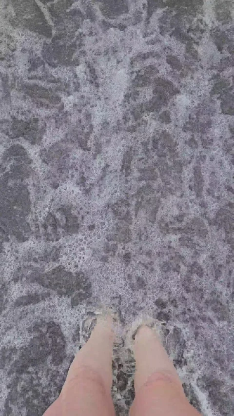 Vertical video of sea waves moving over female feet in black sand 库存影片 337120284