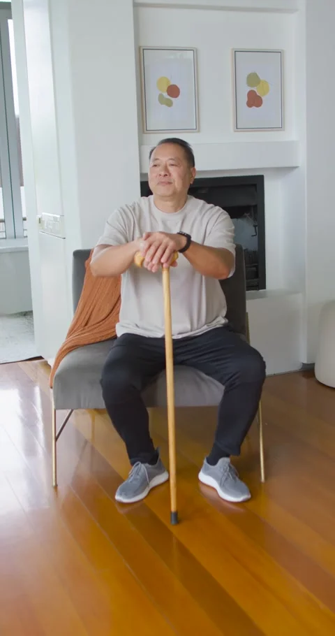 Vertical video: Senior Chinese man sitting holding gold cane in living room, Stock Footage 337734296