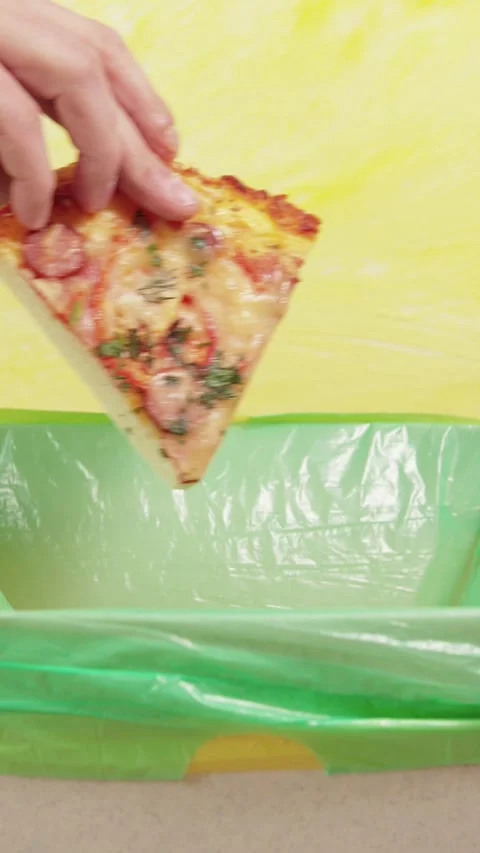 Vertical video shot showing a hand tossing a slice of pizza into a garbage .. Stock Footage 345972607