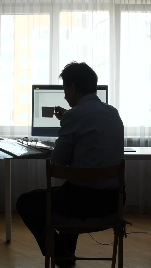 Vertical video silhouette man concentrating on a computer screen, drinking 스톡 동영상 346250871