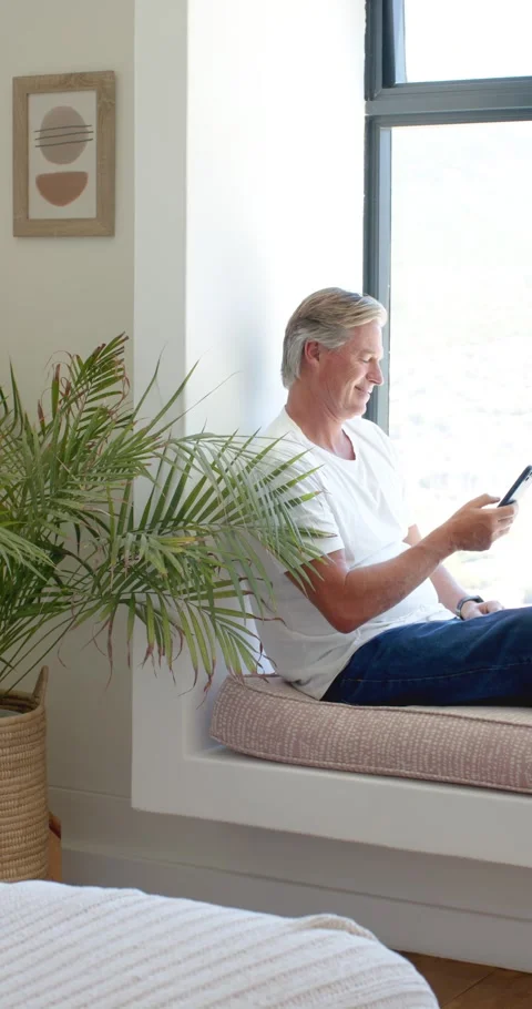 Vertical video: Sitting on bench at home, Senior man in tee, jeans scrolling Stock Footage 345396530