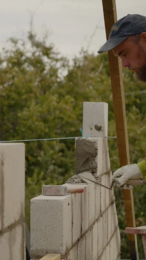 Vertical video Skilled worker constructs a solid wall with concrete bricks for Stock Footage 327602024